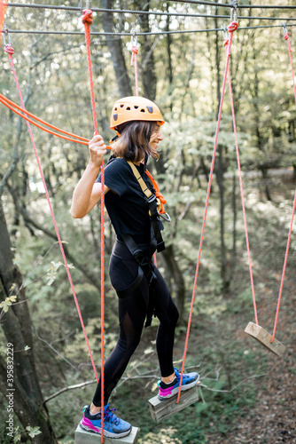 Young well-equipped woman having an active recreation, climbing ropes in the park with obstacles outdoors