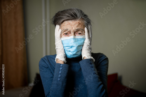 Sad senior woman in protective mask, latex gloves at home during coronavirus pandemic. Stay at home. Old granny retired quarantined epidemic covid 19. Gray hair female in mask infection, bacteria flu