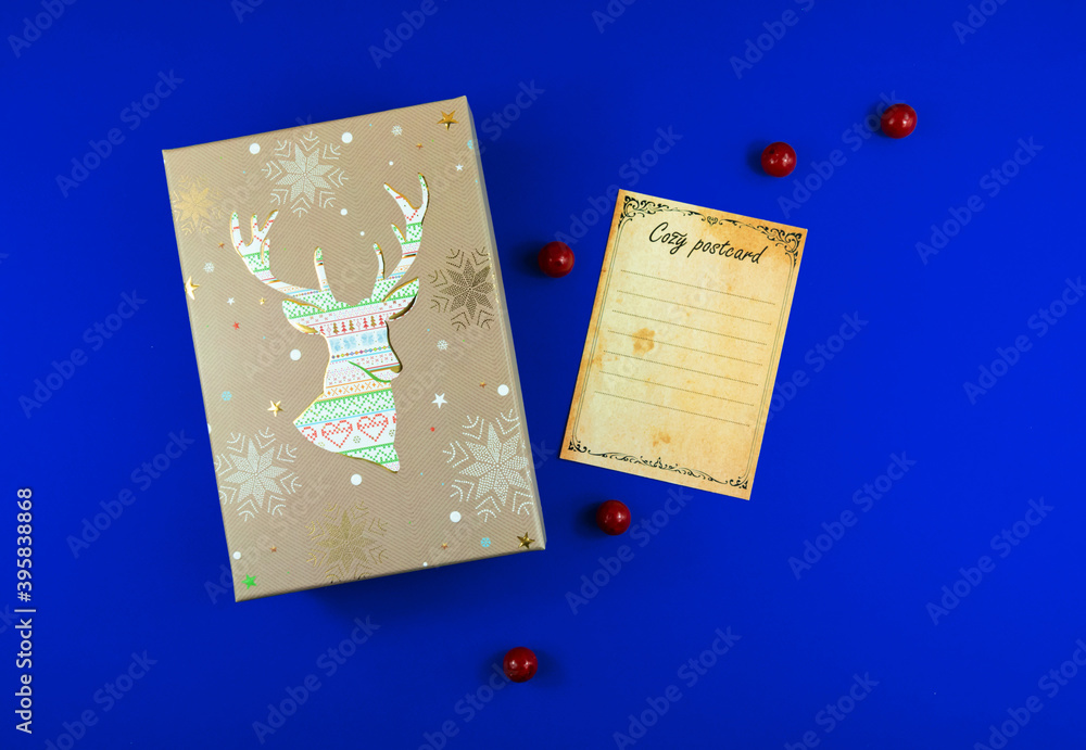 Obraz premium Christmas composition, gift wrap with deer ornament and postcard, blue background, top view