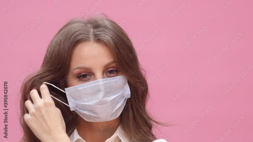 A young lady slowly removes her medical mask while smiling on a pink background. The concept of protection against coronavirus A young lady slowly removes her medical mask while smiling on a pink background. The concept of protection against coronavirus