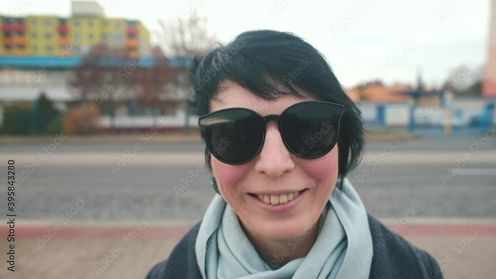 A portrait of a woman in black glasses puts a mask on her face. She smiles. Respiratory protection from dust and dirt in a public place. A portrait of a woman in black glasses puts a mask on her face. She smiles. Respiratory protection from dust and dirt in a public place.