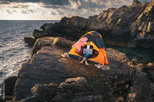 Female sitting in the tent and working on computer. Business woman working from the beach. Working from distance concept. Freelancer travel and work online.
