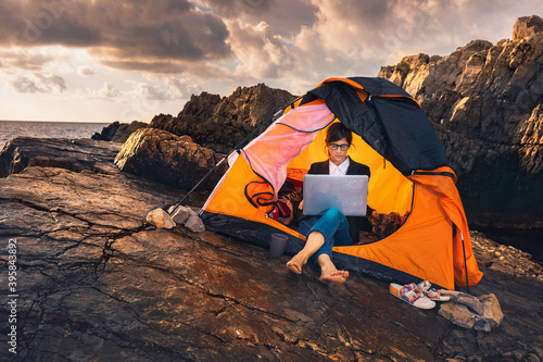 Female sitting in the tent and working on computer. Business woman working from the beach. Working from distance concept. Freelancer travel and work online. photo