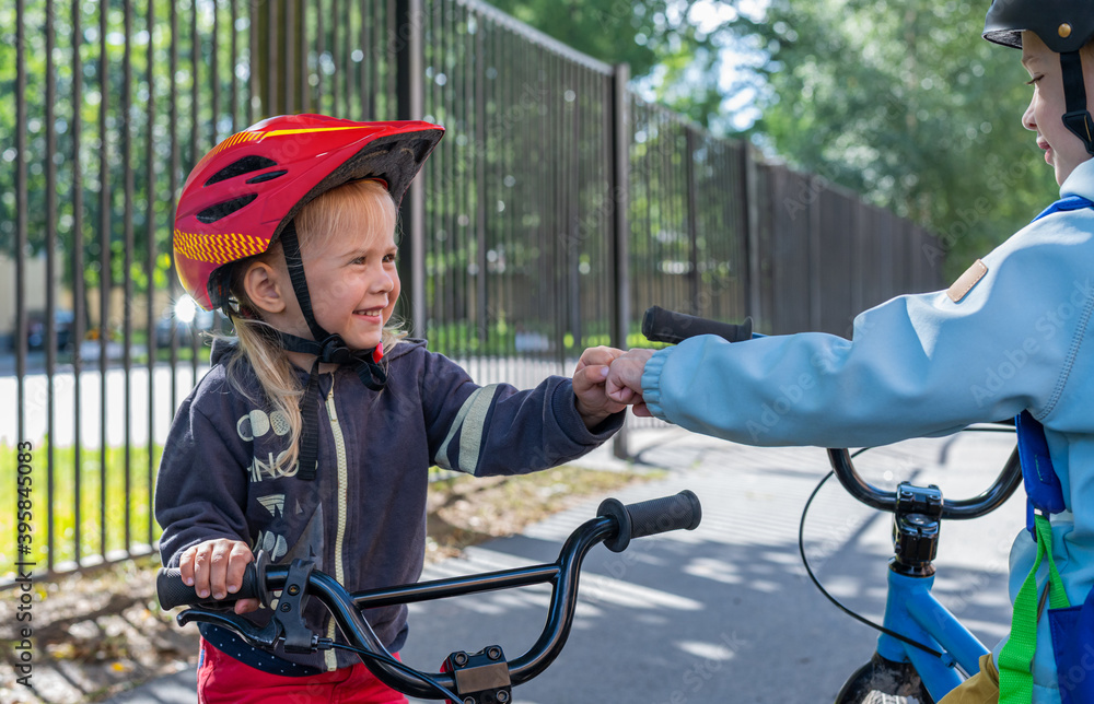 Obraz premium Two children boy and girl greeting each other with fist bump. Friendship, support, equality and diversity. Kids with bicycles are greeting each other on the back yard schools.