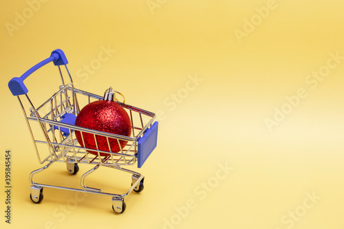 Yellow warm background and a metal cart with one red Christmas ball. Copy Space.