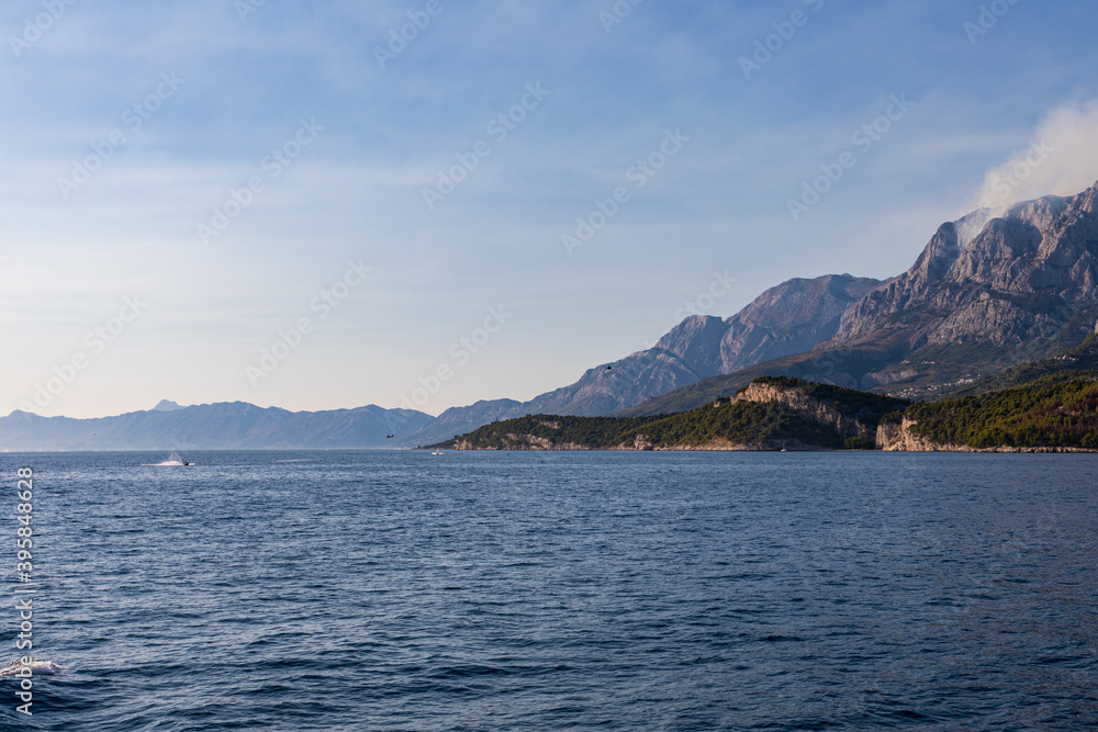 Blick vom Meer auf die Küste in Kroatien. Berge mit Rauchwolken am Himmel