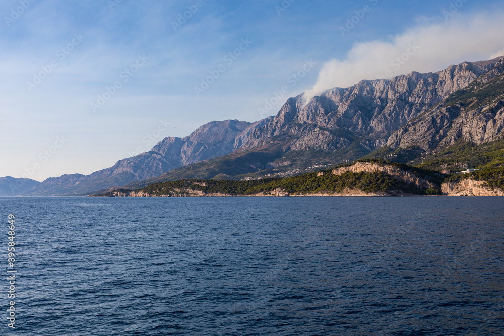 Blick vom Meer auf die Küste in Kroatien. Berge mit Rauchwolken am Himmel