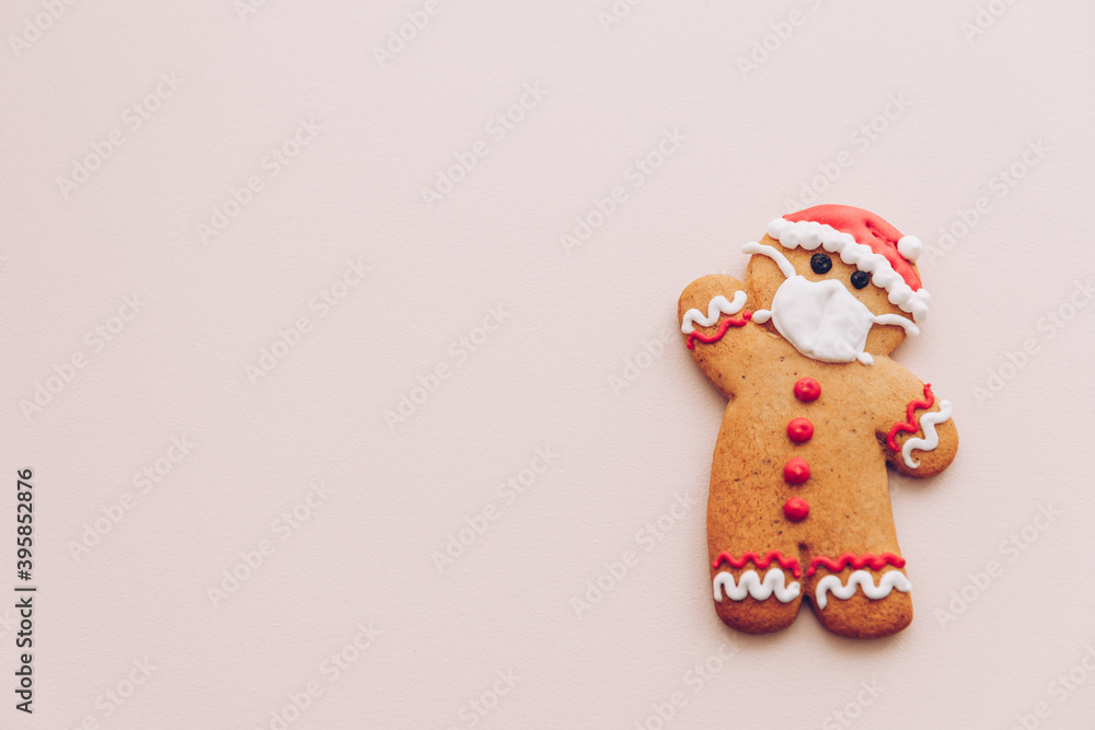 Minimalist Christmas background with gingerbread cookies with the image of a protective medical mask on the face. The concept of celebrating the New Year 2021 in quarantine during a lockdown.