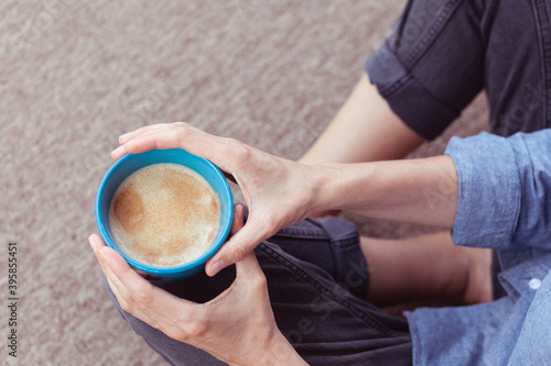 Girl holding coffee mug and sitting on the floor. Woman drinking a cup of coffee or tea sitting cozy at home. Relax and rest. 