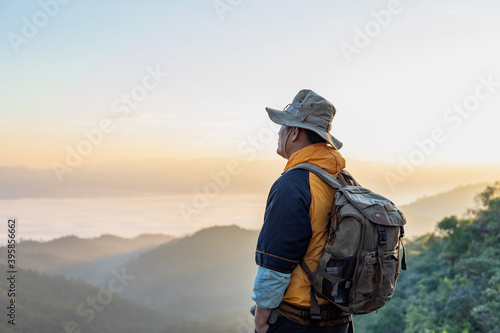 Hipster male hiker with backpack enjoying sunset on peak of foggy mountain. Tourist traveler on background view mockup. © AungMyo