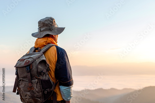 Hipster male hiker with backpack enjoying sunset on peak of foggy mountain. Tourist traveler on background view mockup.