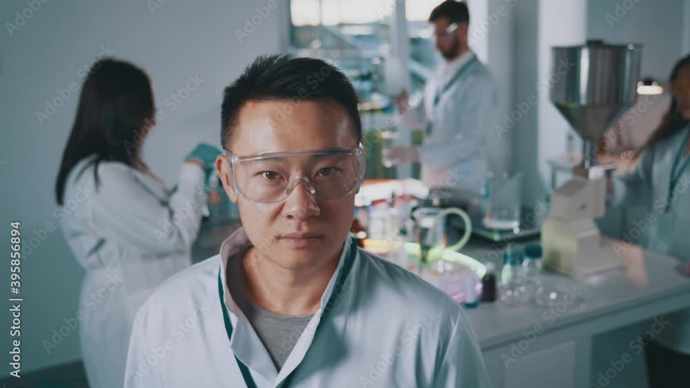 Portrait of asian professional lab worker in white medical gown eyewear standing in busy healthcare office conducting science experiments. Teamwork. Laboratory. Portrait of asian professional lab worker in white medical gown eyewear standing in busy healthcare office conducting science experiments. Teamwork. Laboratory.