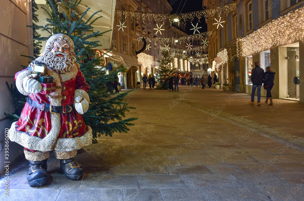 Graz, Austria - November 30, 2019: Santa Claus and beautiful Christmas decorations at night in the city center. Shopping rush during holidays concept, long exposure used for movement effect.
