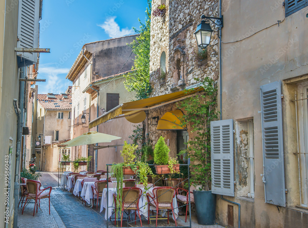 Cozy outdoor restaurant tables at edge of street in narrow alley in coastal town in france