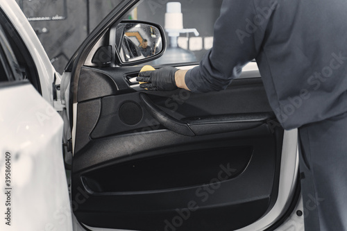 Man in a garage. Worker polish inside a car. Man in a black uniform.