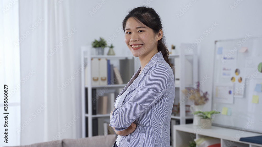 confident asian female manager in professional blazer smiling facing camera is standing with arms crossed in modern office. confident asian female manager in professional blazer smiling facing camera is standing with arms crossed in modern office.