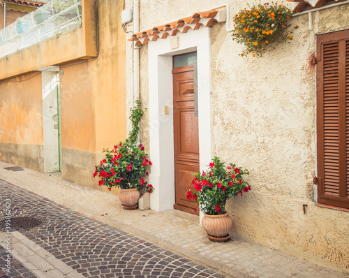 Large pots of pretty red flowers welcome visitors to home on old narrow street in France