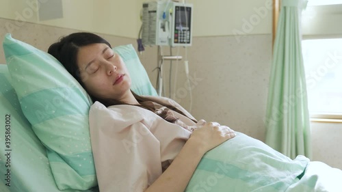 portrait of taiwanese girl leaning alone on bed in ward is having a restless sleep, recovering asian woman is about to wake up after surgery.