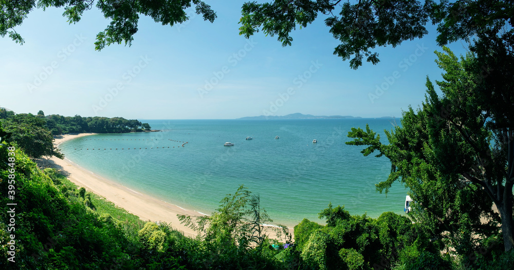 Panorama image of Tropical beautiful seascape view of green trees with blue sea in background at Chonburi, Thailand.