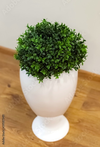 Floor-standing white vase with artificial greenery close-up against the floor and white wall