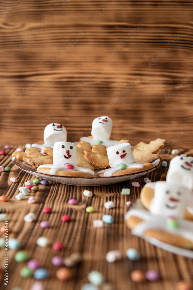 Obraz premium Plätzchen mit Marshmallows, Zuckerguss und Schokolinsen die aussehen wie geschmolzene Schneemänner auf Tellern zur Weihnachtszeit