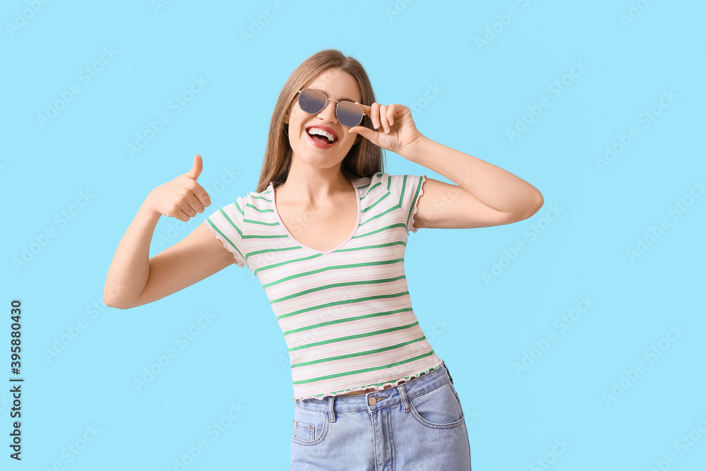 Beautiful woman with stylish sunglasses showing thumb-up gesture on color background Beautiful woman with stylish sunglasses showing thumb-up gesture on color background