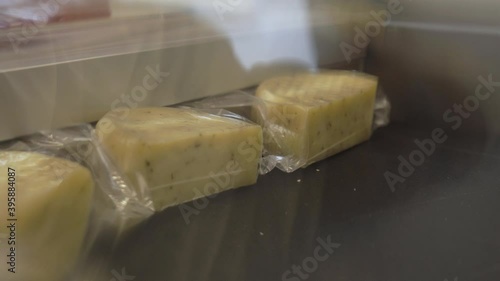 Enterprise, factory production dairy cheese products. Three pieces hard yellow cheese packed in plastic wrap. A vacuum machine sucks air out package. Hermetically packaged cheese products for shops.