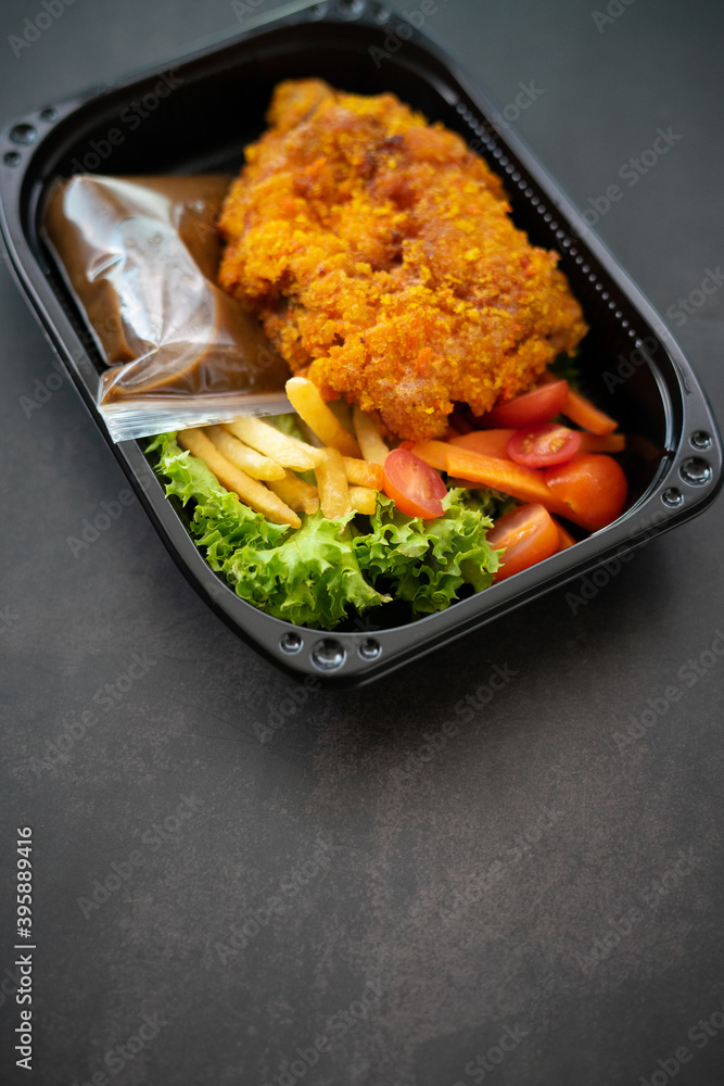 Chicken Chop and fries with Black Pepper sauce and vegetables. in a take away container. Chicken Chop and fries with Black Pepper sauce and vegetables. in a take away container.