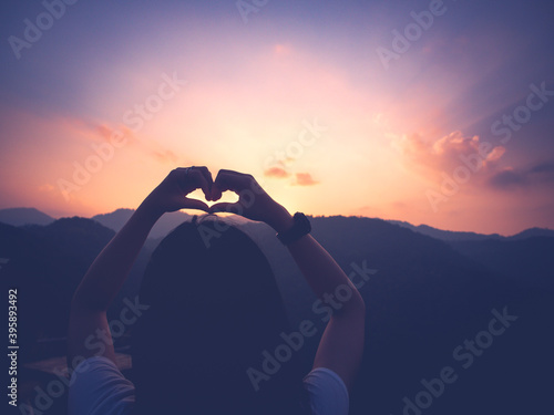 silhouette of young woman making heart shape with hands in the atmosphere sunset on mountain peak..