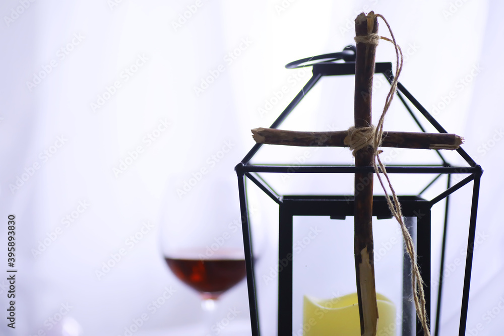 Religious concept. Handmade wooden cross on a white background. Wine glass lamp with candles.