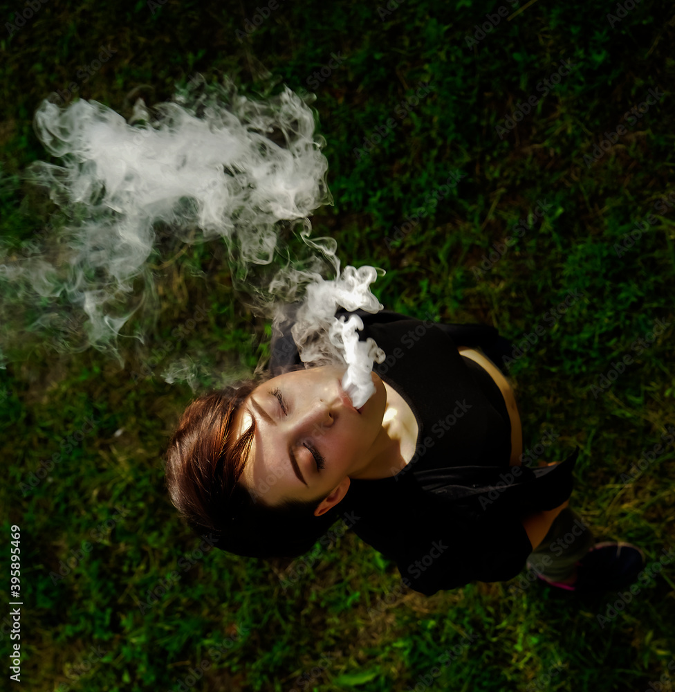 Fotka „young girl smokes electronic cigarette. teenagerl vaping a vaporizer  on green grass background. face of vaping young woman . top view. no  smoking day“ ze služby Stock | Adobe Stock