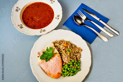 Two plates, one with turkey, pea and buckwheat, second with goulash soup, cutlery and napkin. photo