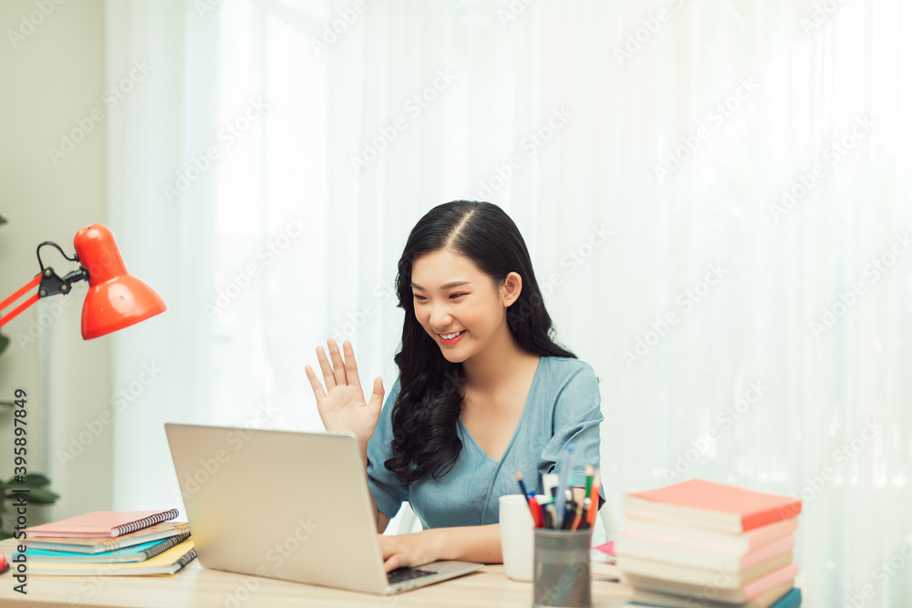 Positive cheerful asian girl have online video call broadcast meet bloggers say hi wave hand sit table use laptop in house indoors Positive cheerful asian girl have online video call broadcast meet bloggers say hi wave hand sit table use laptop in house indoors