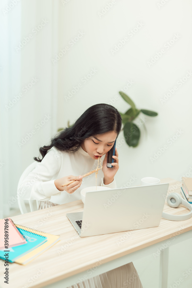 Confident smiling attractive young asian woman entrepreneur having lunch break while sitting at the office desk and using mobile phone Confident smiling attractive young asian woman entrepreneur having lunch break while sitting at the office desk and using mobile phone