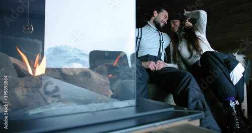 Attractive man and woman in love chilling on a couch. Couple kiss after skiing with a fireplace in frontground 4K photo