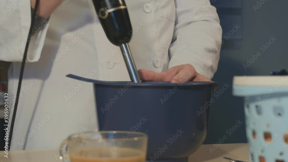 a pastry chef in white clothes whips the cream with a black blendor. The pastry chef explains his actions with comments and hand gestures a pastry chef in white clothes whips the cream with a black blendor. The pastry chef explains his actions with comments and hand gestures