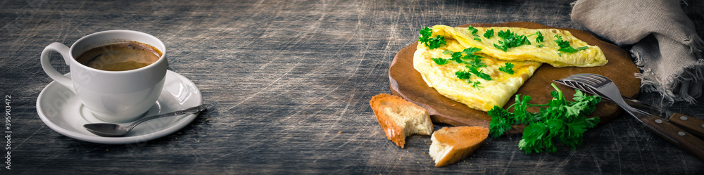Banner a traditional French omelet with toasts and butter, chopped parsley and a white porcelain cup of coffee on a wooden board placed on a dark wooden table and dark wooden background, copy space Banner a traditional French omelet with toasts and butter, chopped parsley and a white porcelain cup of coffee on a wooden board placed on a dark wooden table and dark wooden background, copy space