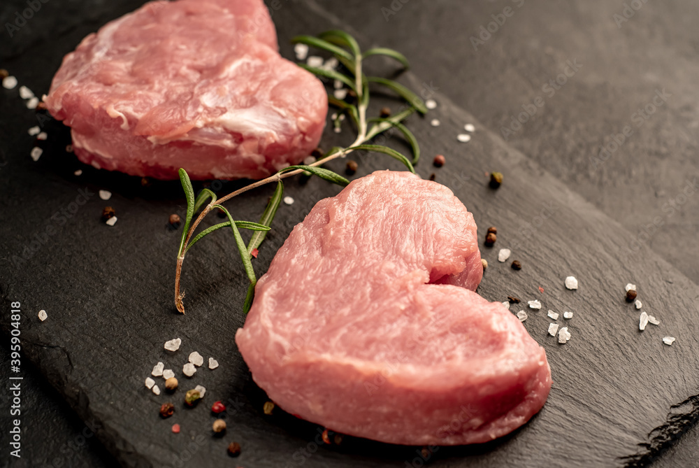 two raw pork steaks in the shape of a heart with spices for Valentine's Day on a stone background two raw pork steaks in the shape of a heart with spices for Valentine's Day on a stone background