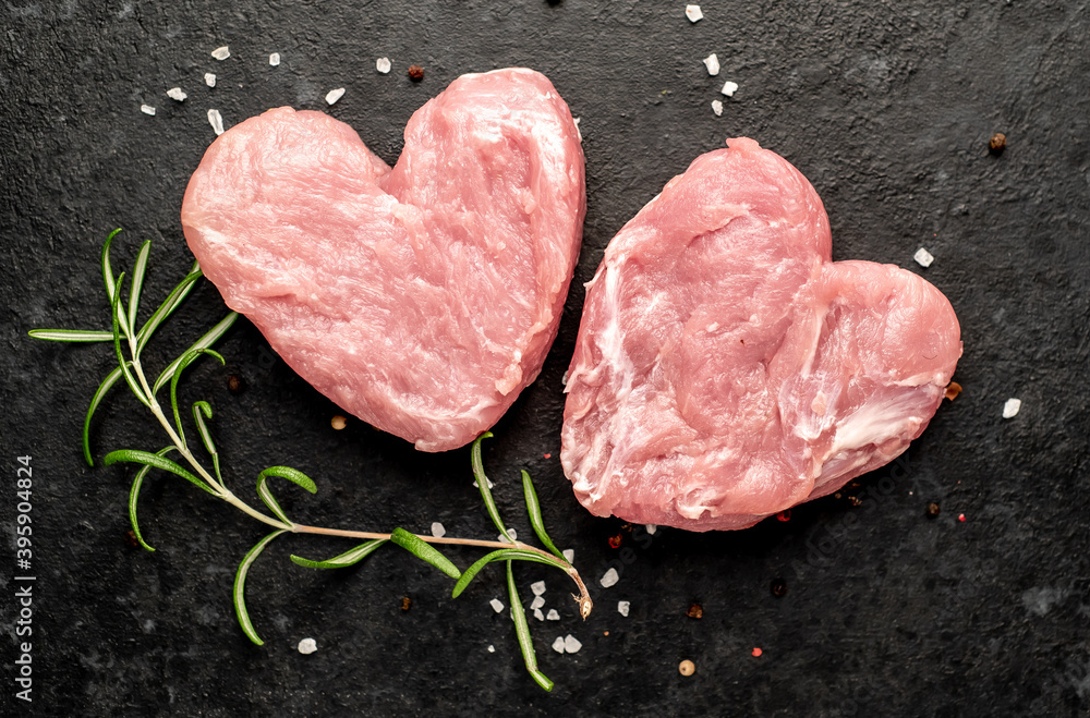 two raw pork steaks in the shape of a heart with spices for Valentine's Day on a stone background
