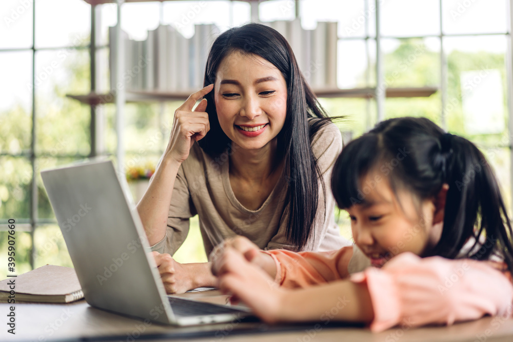 Mother and asian kid little girl learning and looking at laptop computer making homework studying knowledge with online education e-learning system.children video conference with teacher tutor at home Mother and asian kid little girl learning and looking at laptop computer making homework studying knowledge with online education e-learning system.children video conference with teacher tutor at home