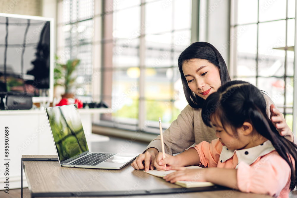 Mother and asian kid little girl learning and looking at laptop computer making homework studying knowledge with online education e-learning system.children video conference with teacher tutor at home Mother and asian kid little girl learning and looking at laptop computer making homework studying knowledge with online education e-learning system.children video conference with teacher tutor at home