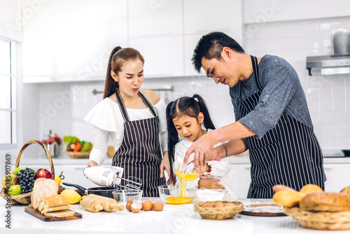 Portrait of enjoy happy love asian family father and mother with little asian girl daughter child having fun cooking together with baking cookies and cake ingredients on table in kitchen