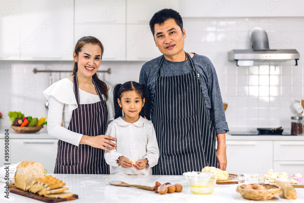 Portrait of enjoy happy love asian family father and mother with little asian girl daughter child having fun cooking together with baking cookies and cake ingredients on table in kitchen