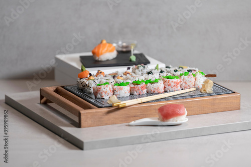 An assortment of uramaki pieces on a tray with chopsticks, with two nigiri pieces on top of planks