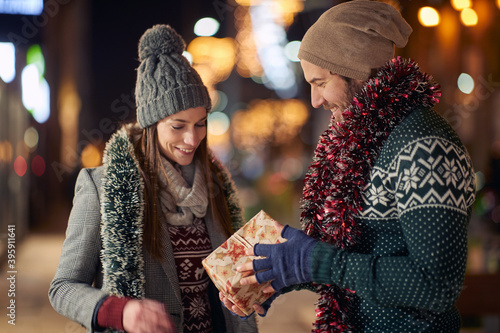 A boyfriend giving Xmas present to his girlfriend while walking the city together. Christmas, relationship, love