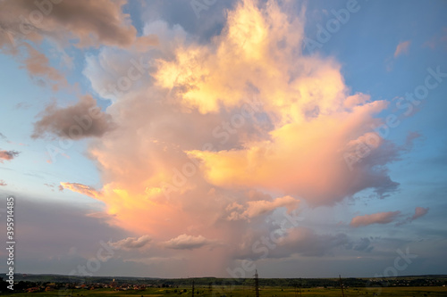 Dramatic stormy sunset over rural area with puffy clouds lit by orange setting sun and blue sky.