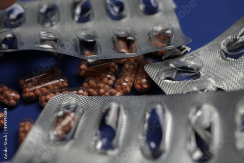 Macro close up of silver empty blisters with pile of capsules, blue background - medicines waste abuse concept