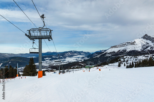 Empty chair lift at french Villard de Lans ski resort surrounded by snowy Vercors mountains.