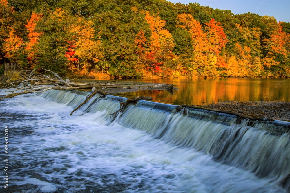 Michigan Autumn Landscape. The Grand River surrounded by vibrant autumn foliage and small waterfall at the Fitzgerald County Park in Grand Ledge, Michigan.