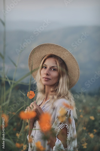 The blonde in a linen dress walks among herbs and wildflowers on a meadow in the mountains. A woman in the Boho style, resting in the countryside, a simple village lifestyle